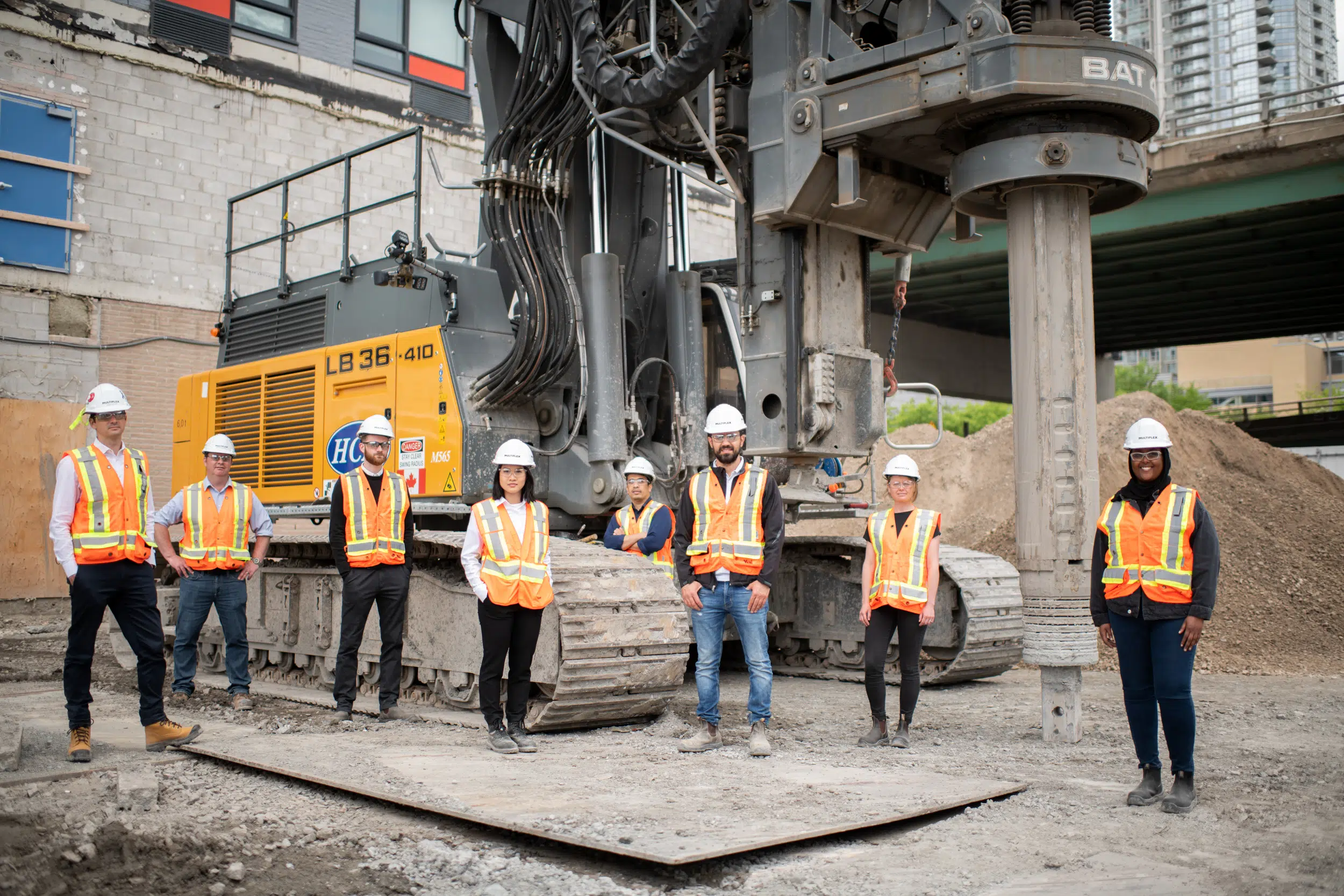 The executive team poses for a group photo next to some heavy equipment. The team is excited to get started on their new project.