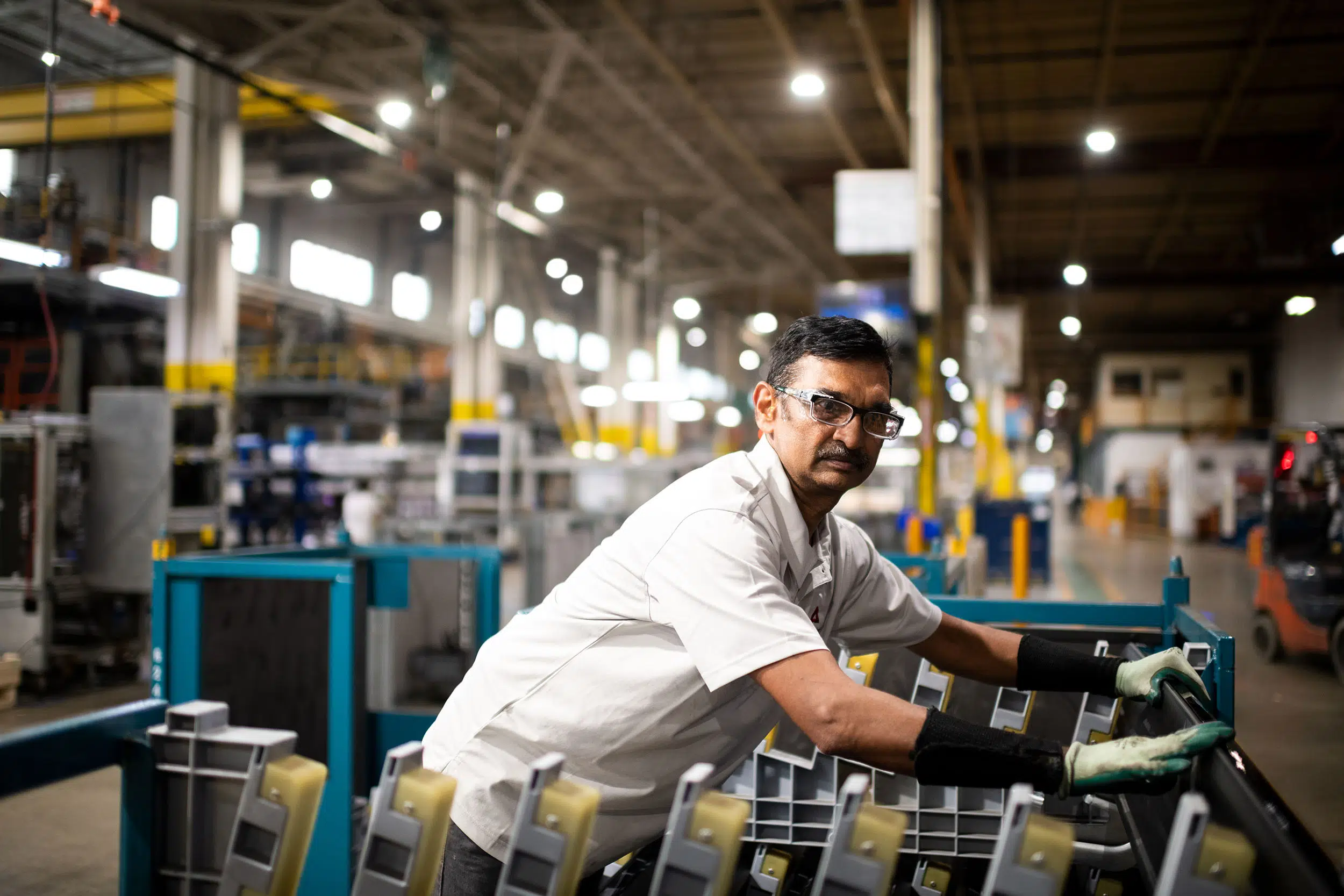 A worker moves new molded bumpers for an automobile into a shipping crate.