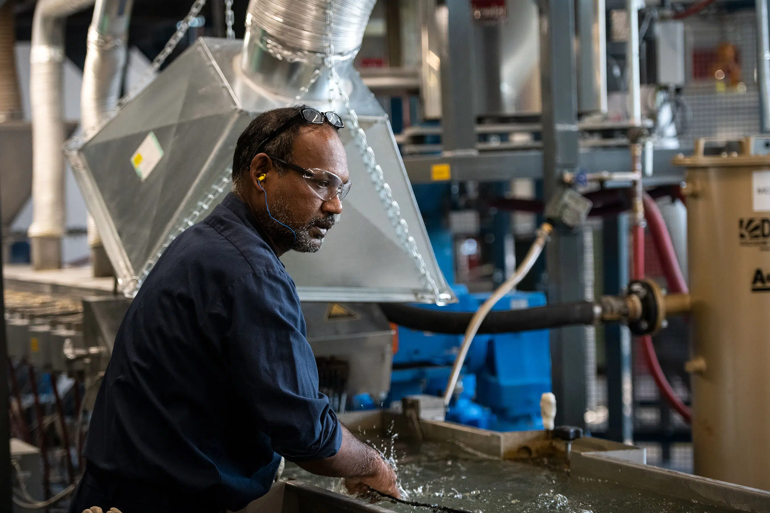 A production worker guides a newly formed string of plastic through a production line.