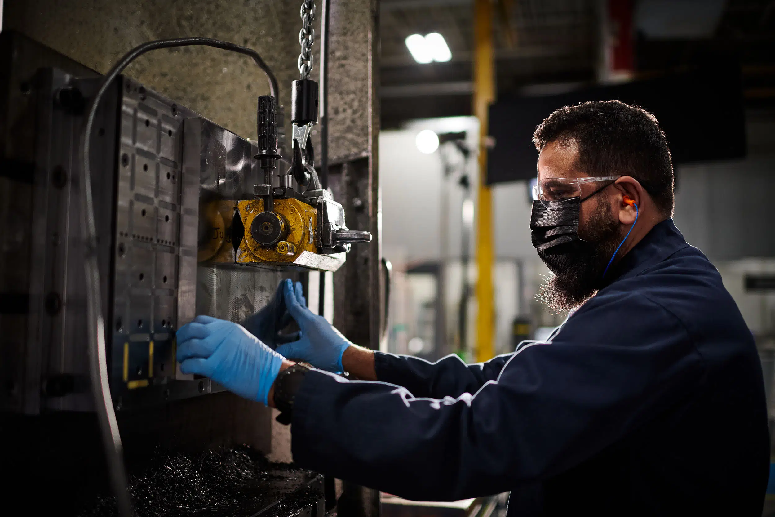 A worker lifts a large piece of metal into the machine with a crane.