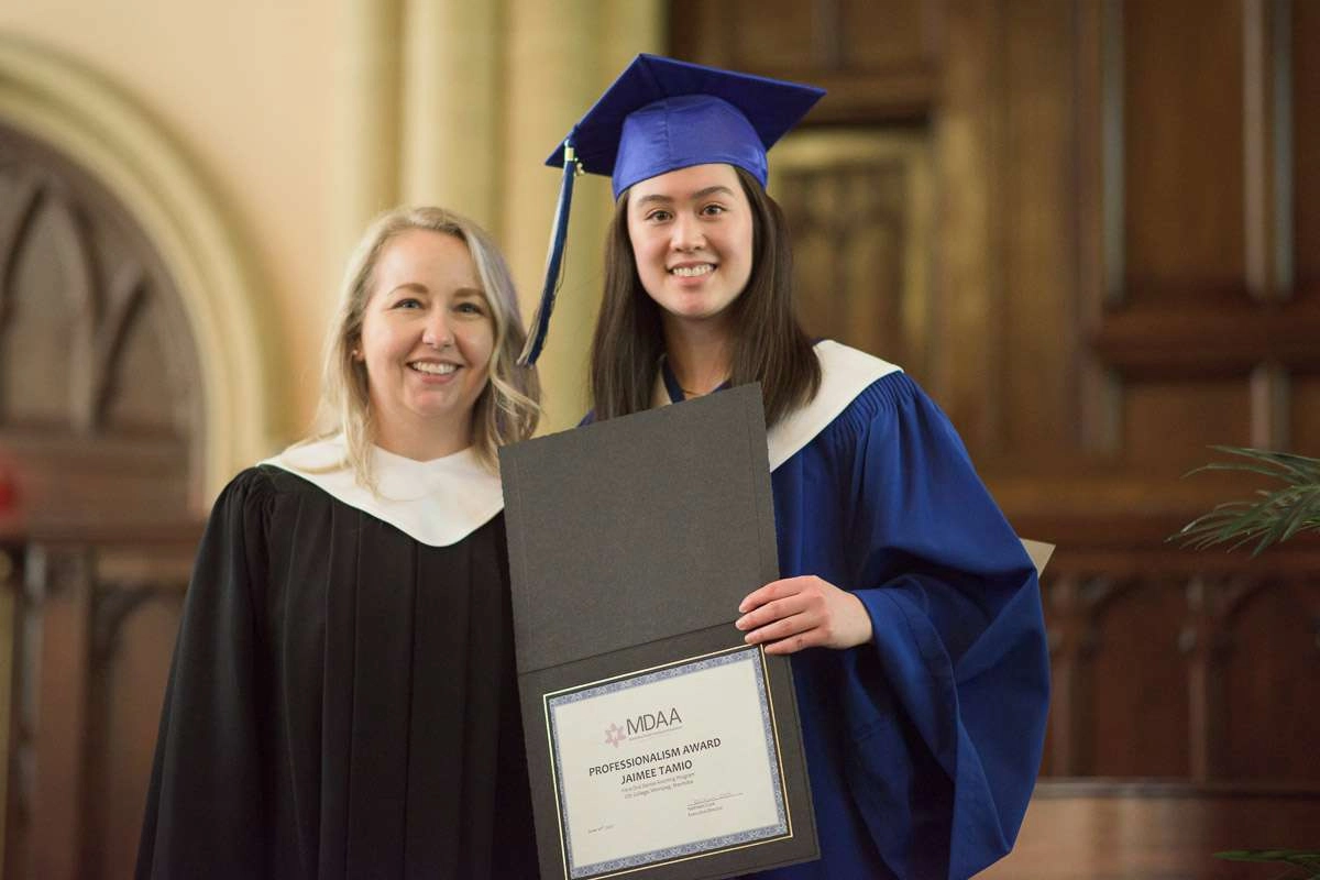 An instructor poses with a student holding an award certificate.