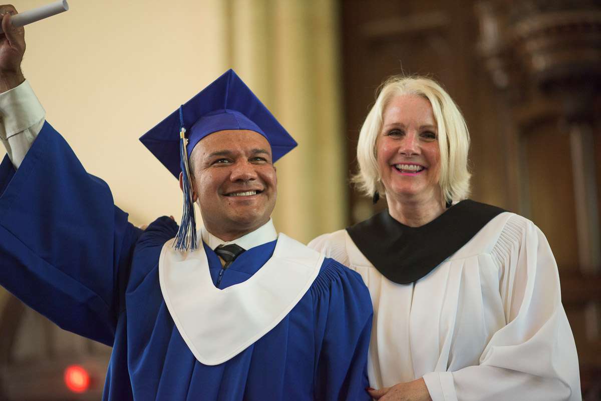 In this action shot, a new graduate raises their diploma, victoriously, with an instructor at their side.