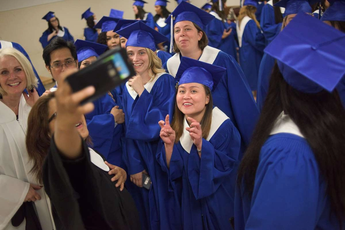 There is a lot of activity in this photograph, which features a group of students and instructors taking a group shot using a phone. The photograph conveys the celebratory atmosphere of the event.