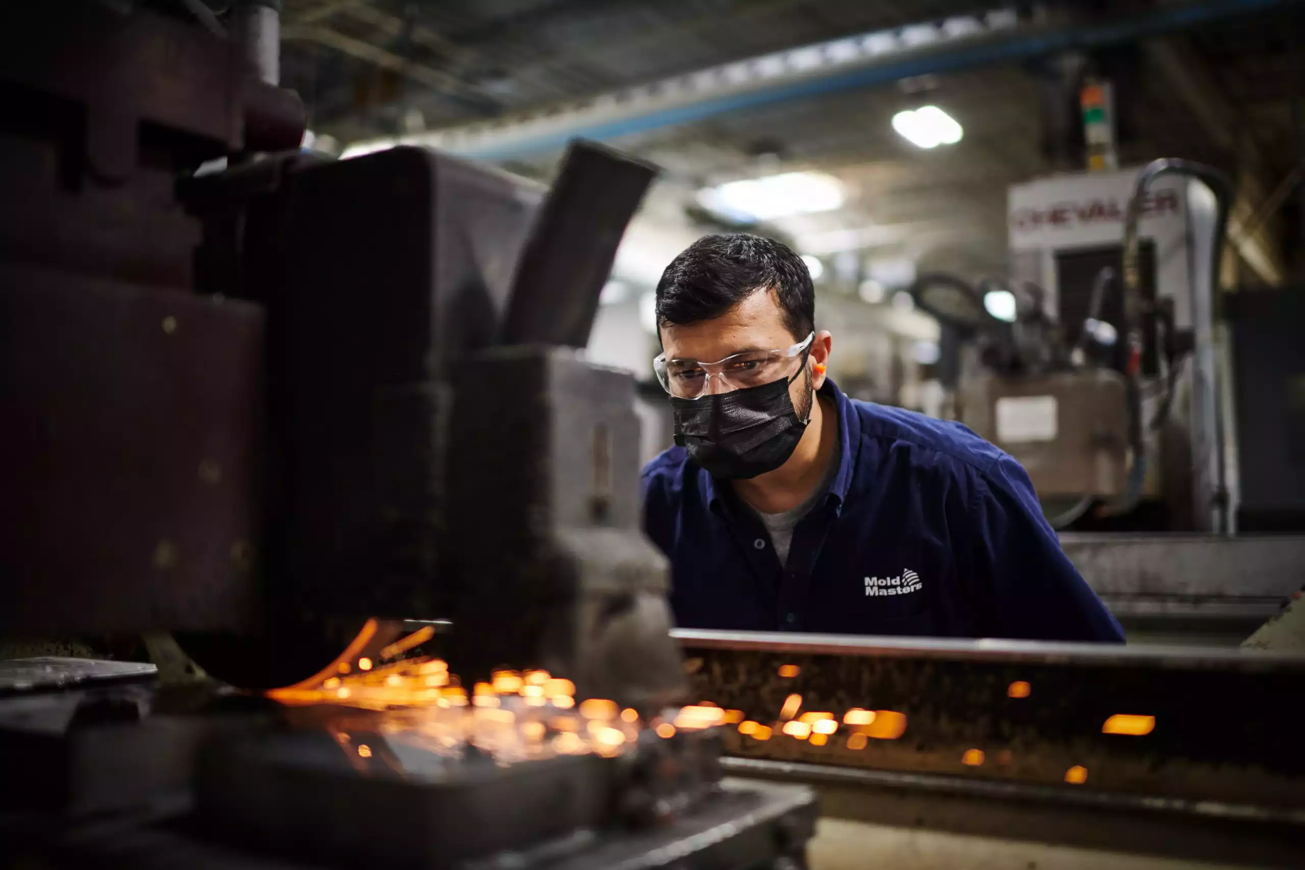 An industrial image of a worker inspecting a part being machined in a factory.