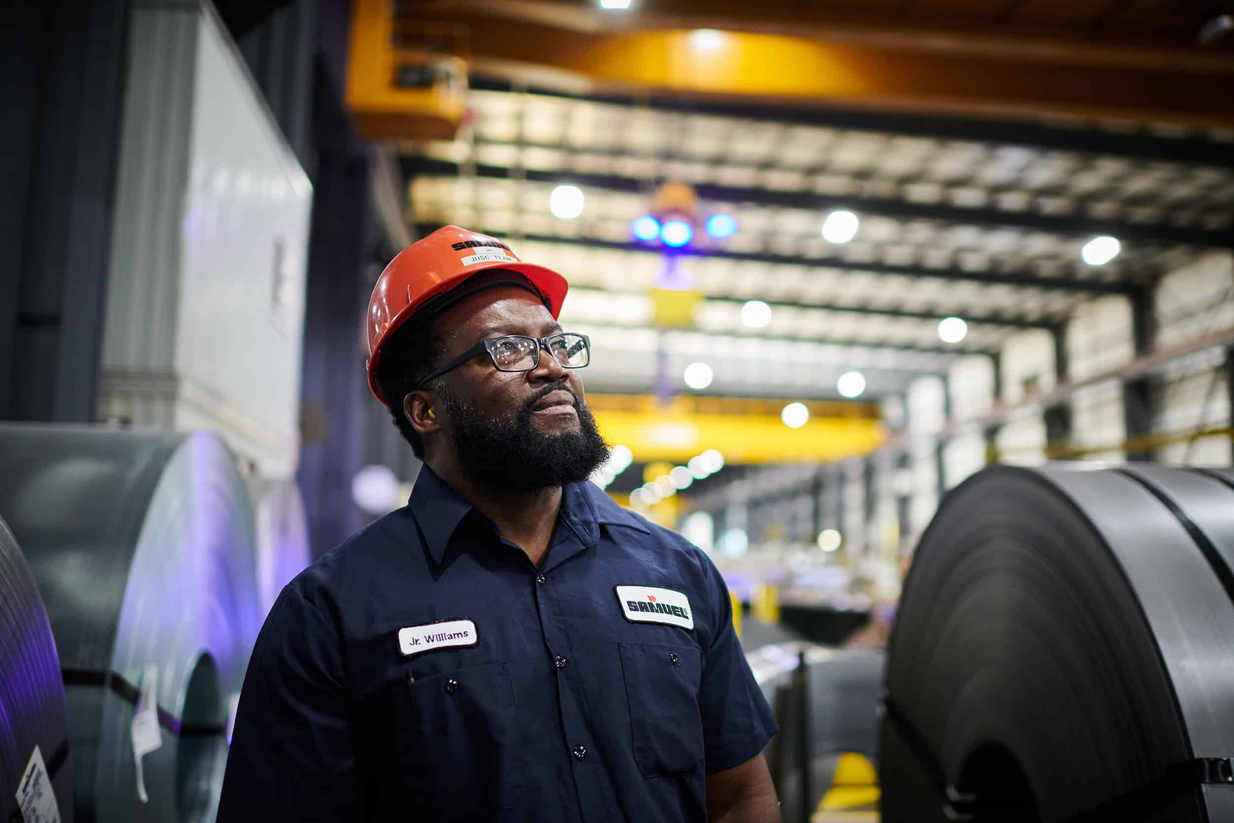 A worker inspects large rolls of metal.